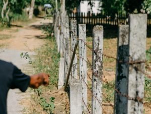 mẫu đơn khởi kiện lấn chiếm đất đai – minh họa hàng rào bê tông và dây thép gai bị lấn chiếm, tay chỉ vào mốc giới tranh chấp đất đai